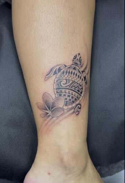Tortue et fleurs de frangipanier en noir et gris sur la cheville