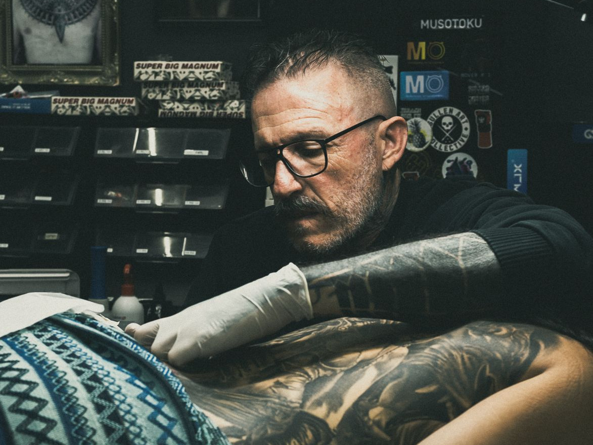 Adrien, gants blancs et machine en main, tatouant un dos sur un champ propre dans son studio de Nouméa