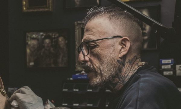 Adrien au travail dans son studio de Nouméa Adrien de profil, lunettes et machine en main, tatouant l'épaule d'une cliente dans son studio de Nouméa