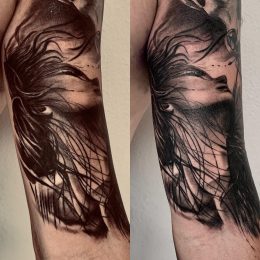 Visage de femme et plumes en noir et gris sur le bras
