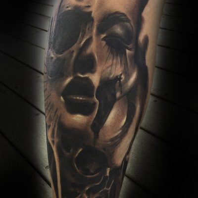 Visage et crâne en noir et gris sur le bras