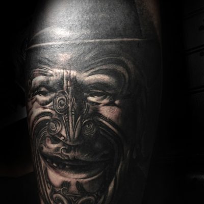 Masque maori sculpté en noir et gris sur le bras