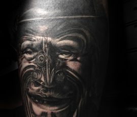 Masque maori sculpté en noir et gris sur le bras