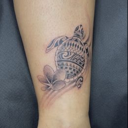 Tortue et fleurs de frangipanier en noir et gris sur la cheville