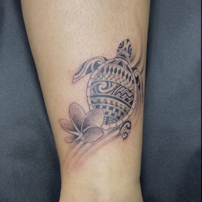 Tortue et fleurs de frangipanier en noir et gris sur la cheville