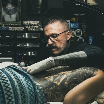 Adrien penché sur un dos en cours de tatouage, dans son studio de Nouméa aux murs couverts de cadres